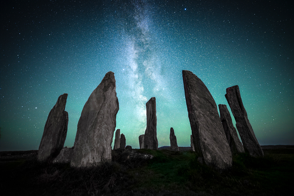 Standing stones with the night sky illuminated in blue and the Milky Way in the middle